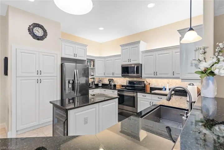 Kitchen featuring dark stone counters, decorative backsplash, sink, appliances with stainless steel finishes, and wine cooler
