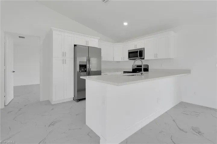 Modern kitchen featuring an island with a breakfast bar, stainless steel appliances, white cabinetry with brushed nickel hardware, light-toned countertops, and light gray tile flooring
