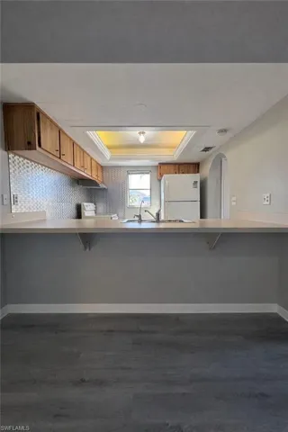 Kitchen with a tray ceiling, a breakfast bar, a peninsula, and white appliances
