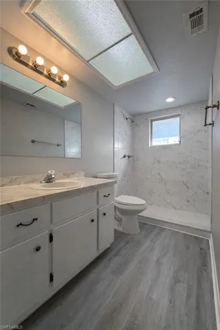 Bathroom featuring a marble finish shower, vanity, and light wood-style floors