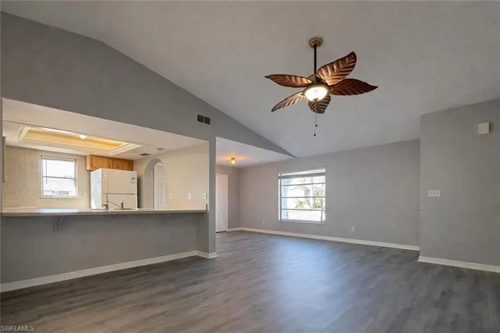 Unfurnished living room featuring vaulted ceiling, plenty of natural light, dark wood finished floors, and ceiling fan