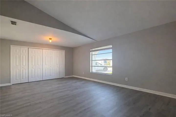 Unfurnished bedroom with vaulted ceiling, a closet, and dark wood-style floors