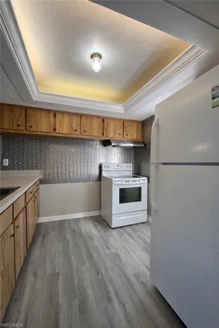 Kitchen featuring a tray ceiling, white appliances, light countertops, brown cabinets, and light wood-style flooring