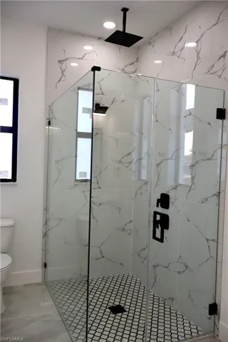Bathroom with a marble finish shower, healthy amount of natural light, and light marble finish flooring