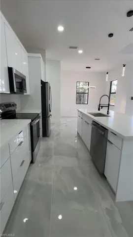 Kitchen with modern cabinets, stainless steel appliances, hanging light fixtures, white cabinets, and a kitchen island with sink