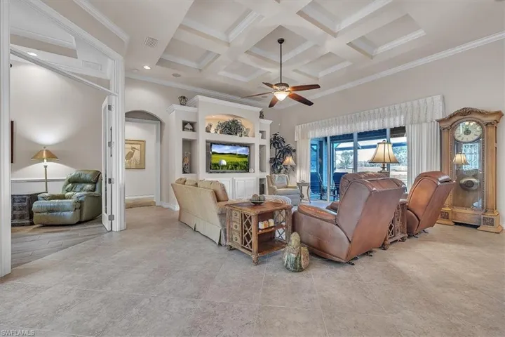 Living room featuring coffered ceiling, a ceiling fan, beam ceiling, ornamental molding, and arched walkways