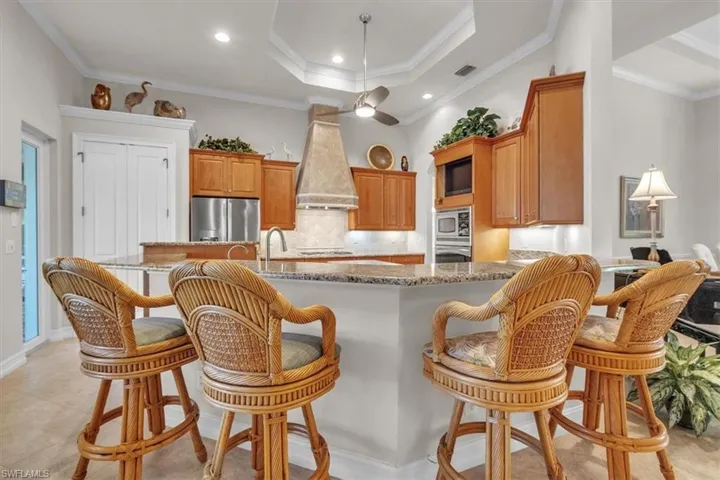Kitchen featuring a breakfast bar area, decorative backsplash, dark stone counters, a peninsula, and crown molding