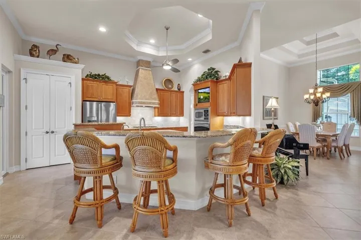 Kitchen featuring a tray ceiling, backsplash, a breakfast bar, light stone countertops, and crown molding