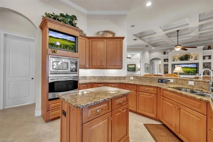 Kitchen with coffered ceiling, brown cabinets, arched walkways, light stone counters, and appliances with stainless steel finishes