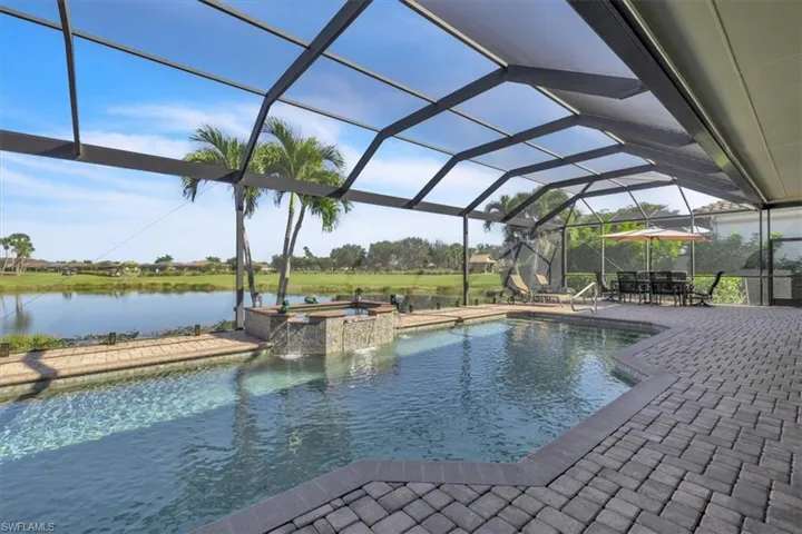 View of pool featuring glass enclosure, a sunroom, a pool with connected hot tub, a patio area, and a water view