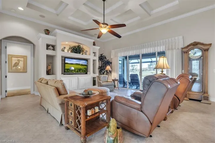Living room with built in shelves, coffered ceiling, ceiling fan, crown molding, and beam ceiling