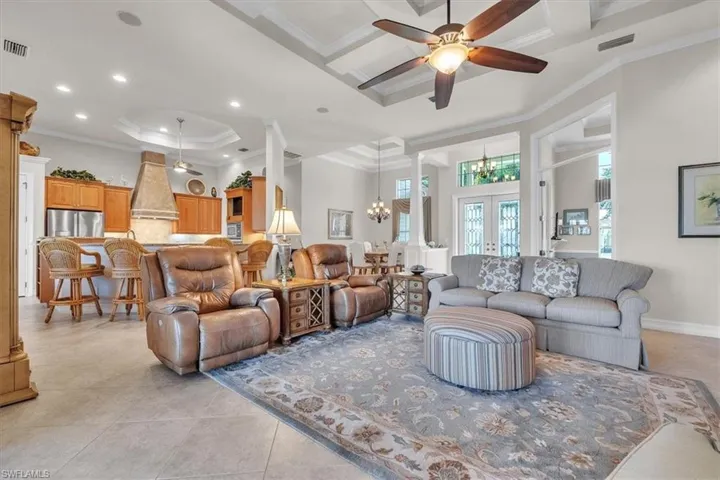Living room featuring decorative columns, a chandelier, a ceiling fan, a tray ceiling, and ornamental molding