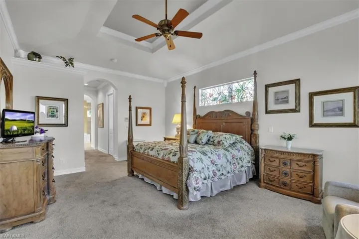 Bedroom with ceiling fan, light carpet, crown molding, a tray ceiling, and arched walkways