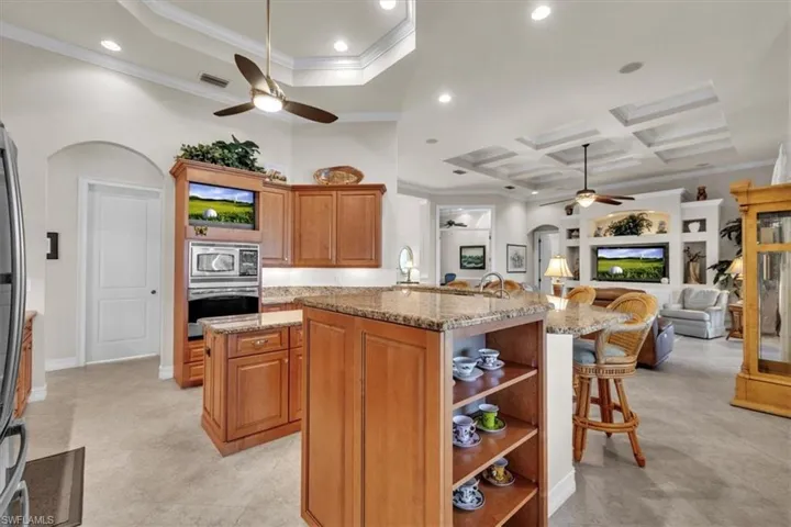 Kitchen with open shelves, a kitchen breakfast bar, light stone counters, ornamental molding, and ceiling fan