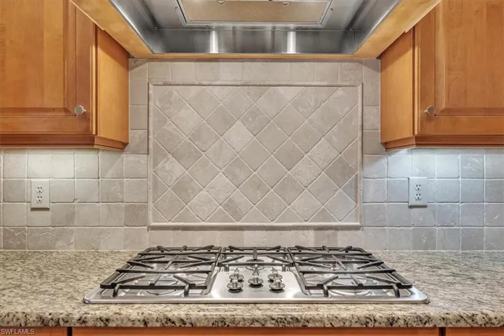 Kitchen featuring exhaust hood, stainless steel gas cooktop, backsplash, and brown cabinets