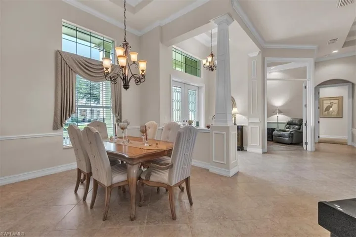 Dining area featuring french doors, ornate columns, crown molding, light tile patterned floors, and a chandelier