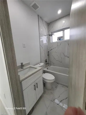 Full bath featuring vanity, light marble finish flooring, and a combined bath / shower with marble appearance