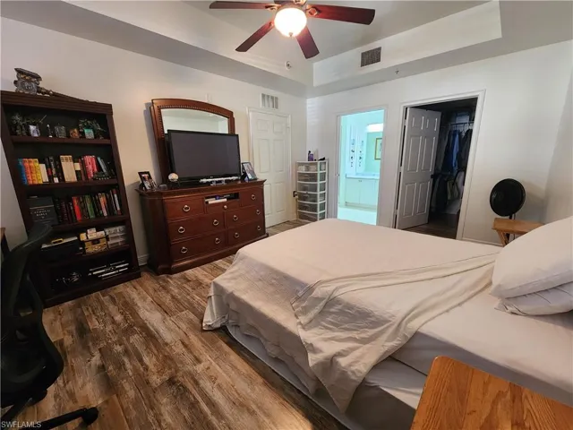 Bedroom with ensuite bath, a spacious closet, wood-type flooring, a closet, and ceiling fan