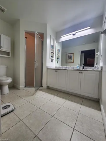 Bathroom featuring a shower with door, tile flooring, vanity, and toilet