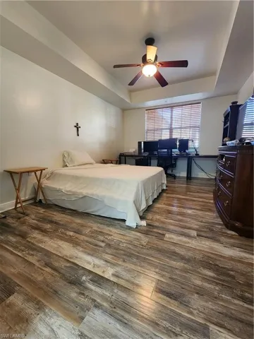 Bedroom featuring dark hardwood / wood-style floors, ceiling fan, and a raised ceiling