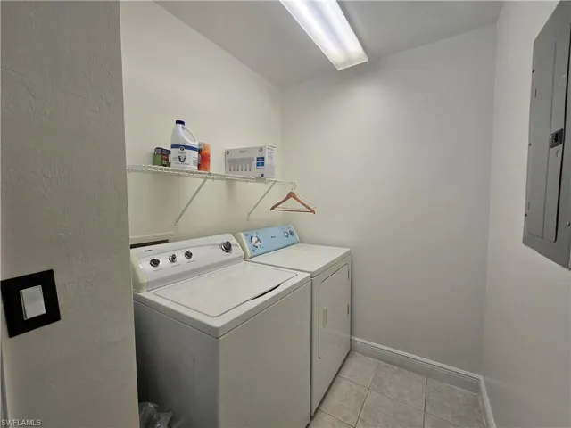 Laundry area featuring washing machine and clothes dryer, electric panel, and light tile patterned floors