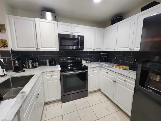 Kitchen with stainless steel appliances, tasteful backsplash, white cabinetry, light stone countertops, and light tile floors