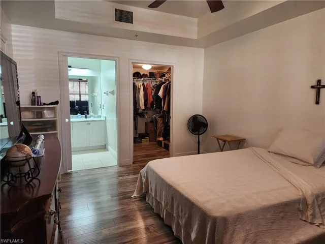 Bedroom with dark hardwood / wood-style floors, a spacious closet, a closet, ensuite bathroom, and ceiling fan