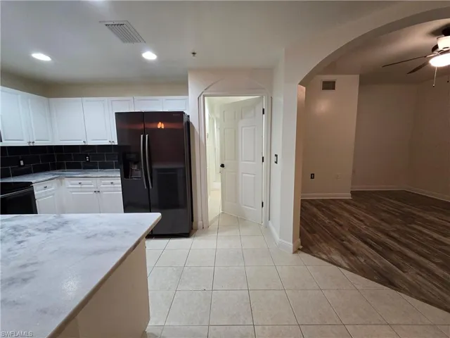 Kitchen with tasteful backsplash, white cabinets, black appliances, light hardwood / wood-style flooring, and ceiling fan