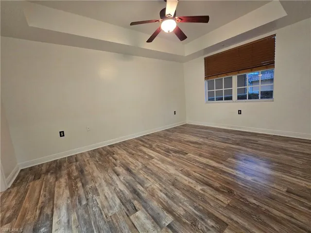 Empty room featuring a tray ceiling, dark wood-type flooring, and ceiling fan