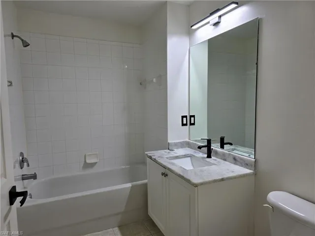 Full bathroom with vanity, tiled shower / bath combo, toilet, and tile patterned flooring