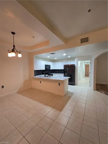 Kitchen featuring white cabinetry, light tile patterned flooring, kitchen peninsula, fridge, and decorative light fixtures