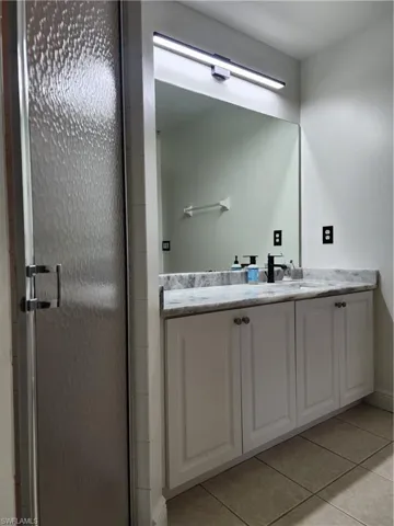 Bathroom with tile flooring, a shower with shower door, and vanity