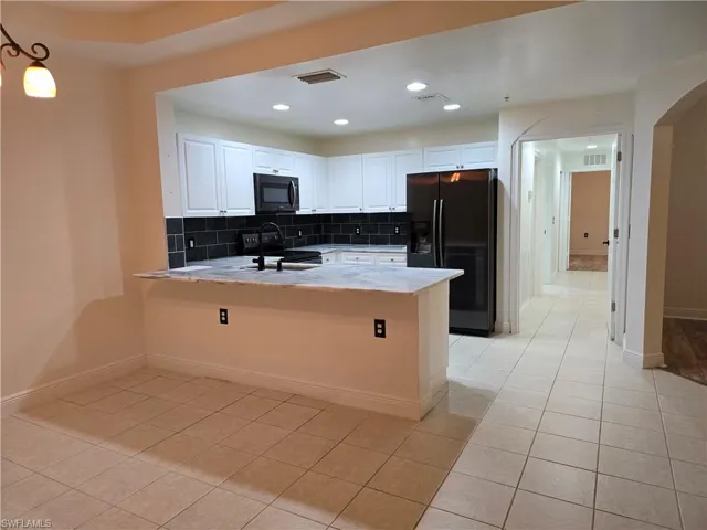 Kitchen featuring white cabinets, backsplash, kitchen peninsula, light tile patterned floors, and black appliances