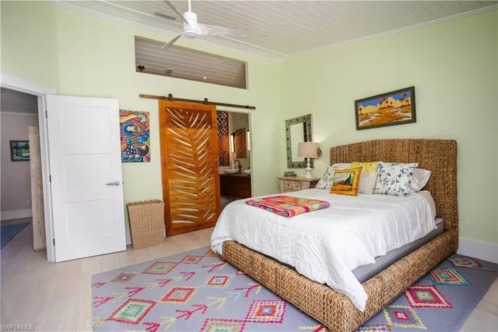 Bedroom with a barn door, ornamental molding, wood finished floors, ensuite bath, and ceiling fan