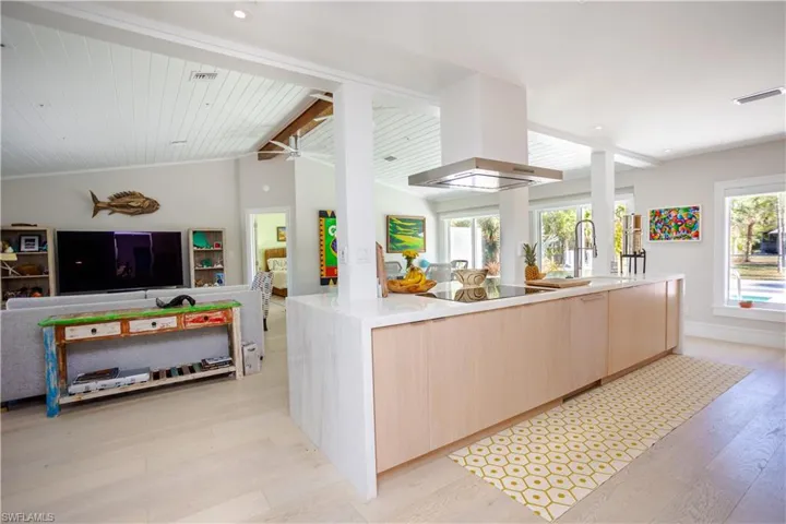 Kitchen with light brown cabinetry, modern cabinets, black electric stovetop, open floor plan, and light wood finished floors