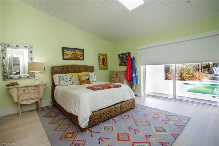 Bedroom with a skylight, wood finished floors, lofted ceiling, access to exterior, and ornamental molding