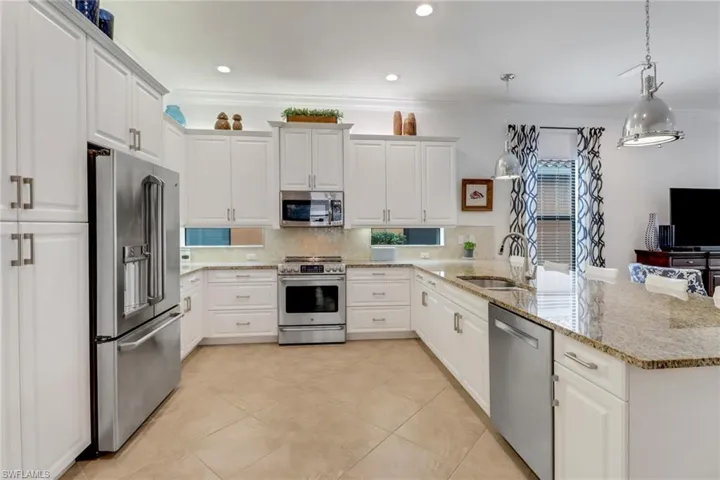 Kitchen featuring light stone countertops, stainless steel appliances, sink, white cabinets, and hanging light fixtures
