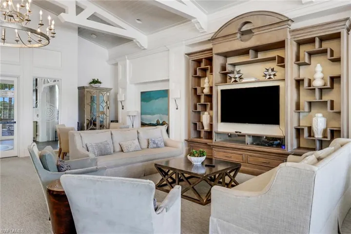 Living room featuring crown molding, carpet floors, lofted ceiling with beams, and a notable chandelier