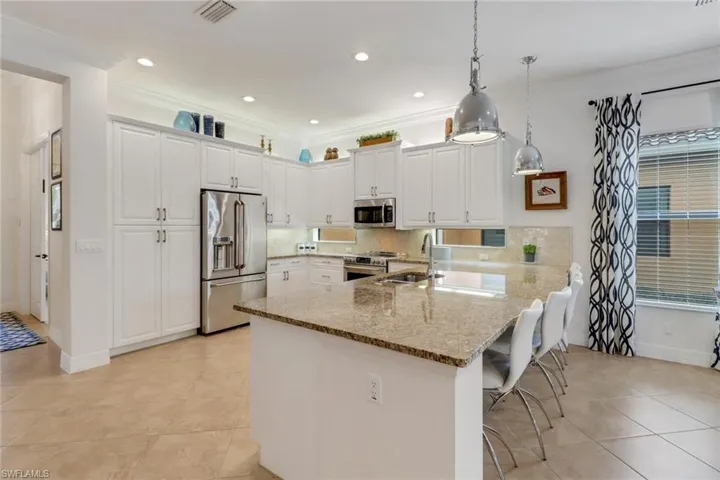 Kitchen featuring white cabinetry, kitchen peninsula, decorative light fixtures, a kitchen bar, and appliances with stainless steel finishes
