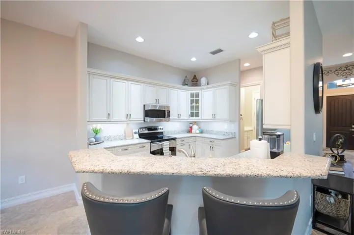 Kitchen with glass insert cabinets, a kitchen bar, white cabinetry, stainless steel appliances, and light stone counters