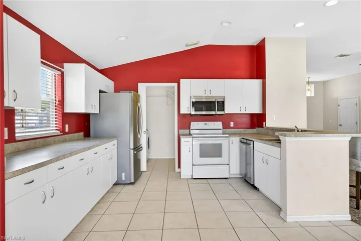 Kitchen featuring white cabinetry, appliances with stainless steel finishes, light tile patterned floors, lofted ceiling, and recessed lighting