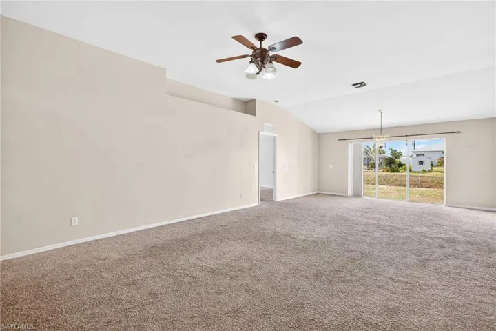 Carpeted empty room featuring vaulted ceiling and a ceiling fan