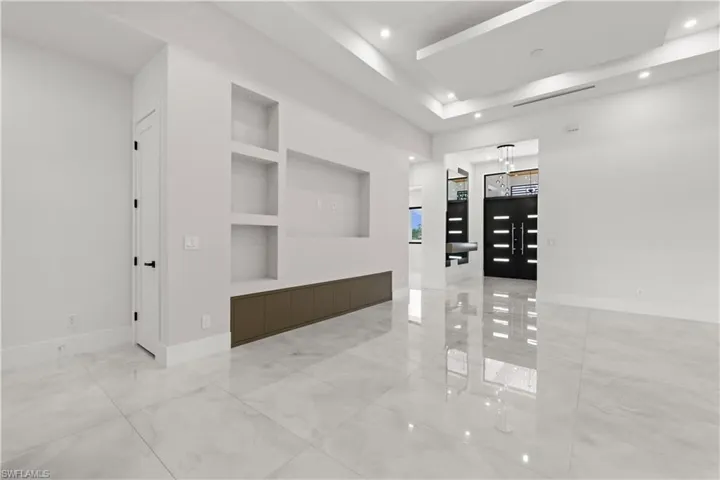 Unfurnished room featuring built in features, light marble finish flooring, a tray ceiling, and recessed lighting