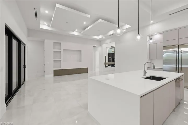 Kitchen featuring modern cabinets, a tray ceiling, an island with sink, open floor plan, and hanging light fixtures