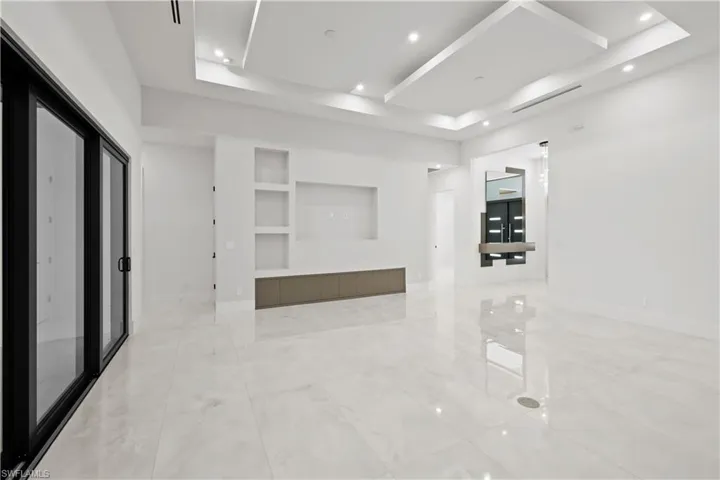 Unfurnished room with a tray ceiling, built in shelves, light marble finish flooring, and recessed lighting