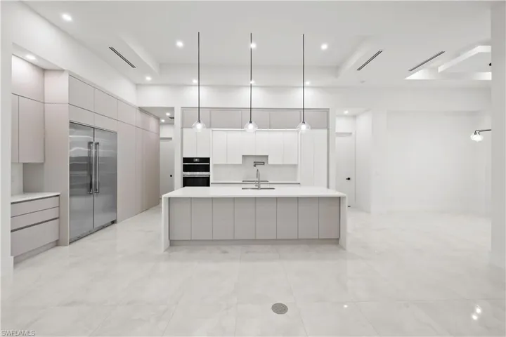 Kitchen with decorative light fixtures, modern cabinets, stainless steel appliances, a kitchen island with sink, and light stone counters