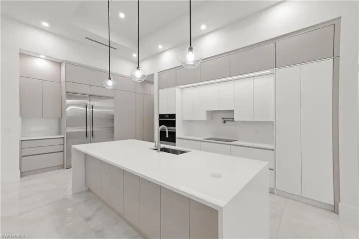 Kitchen featuring modern cabinets, stainless steel appliances, light stone counters, decorative light fixtures, and recessed lighting