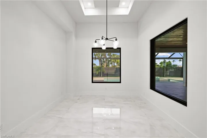 Unfurnished room featuring healthy amount of natural light, marble finish flooring, a chandelier, recessed lighting, and a raised ceiling