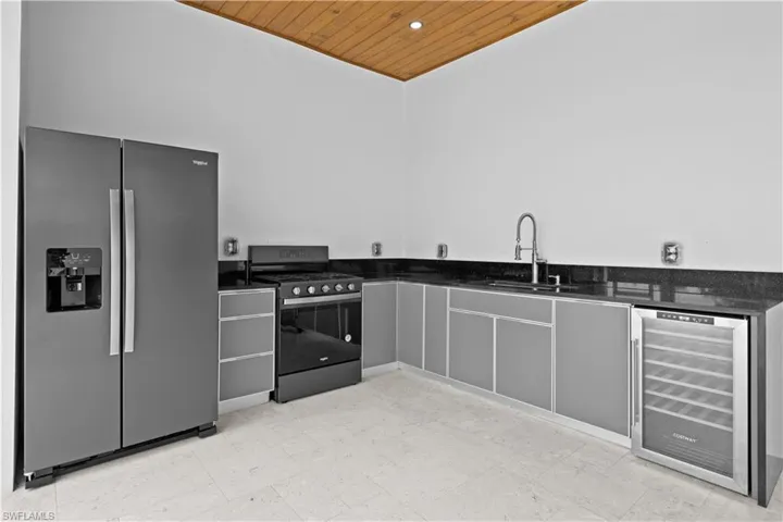 Kitchen with stainless steel appliances, wine cooler, wood ceiling, light flooring, and dark stone countertops
