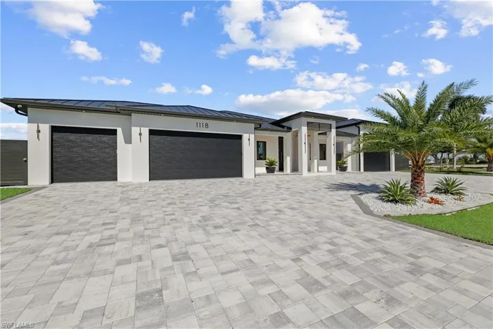 View of front of property with decorative driveway, a garage, a standing seam roof, and stucco siding